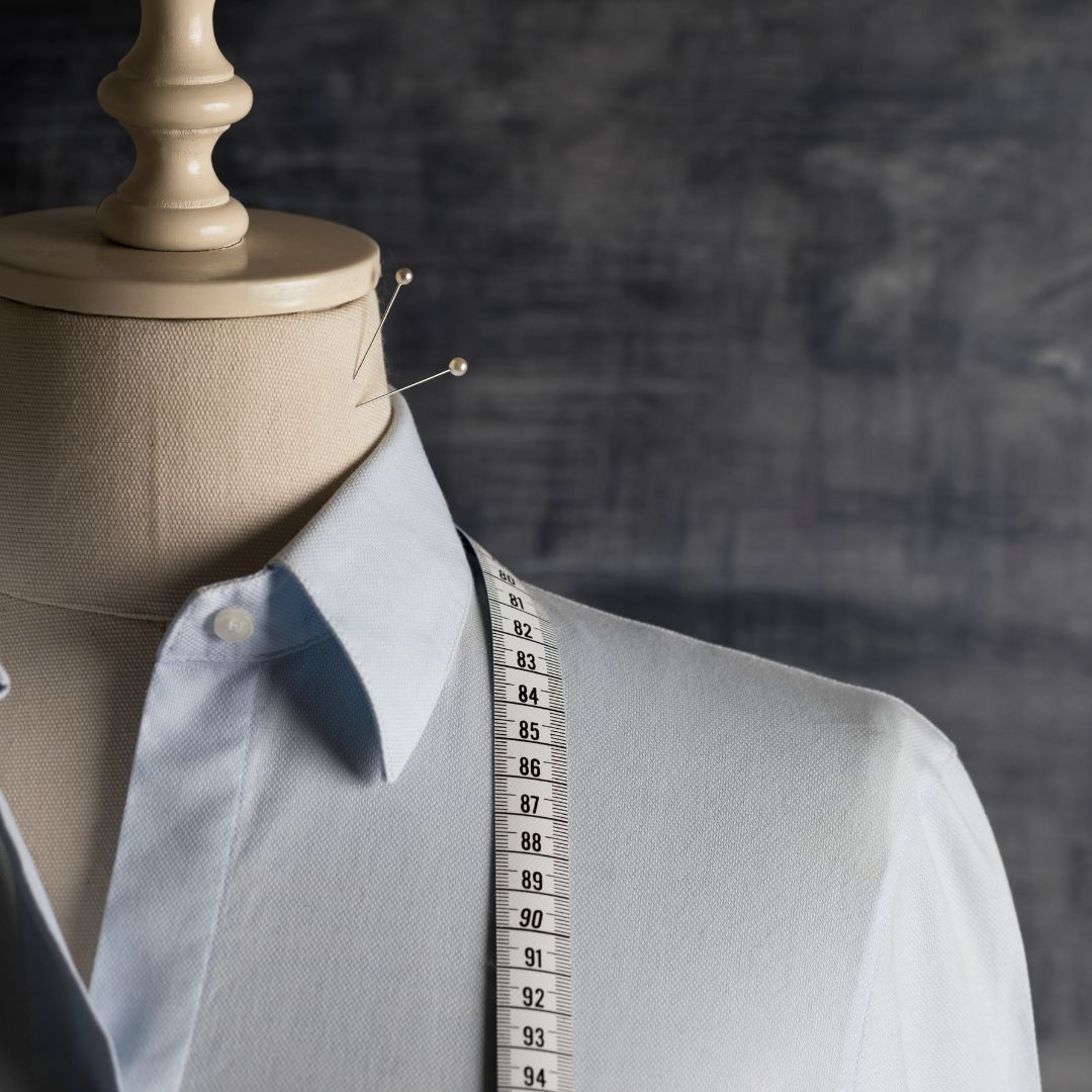 Dress form with a pale blue button-up shirt.  A measuring tape is draped across the shoulder.